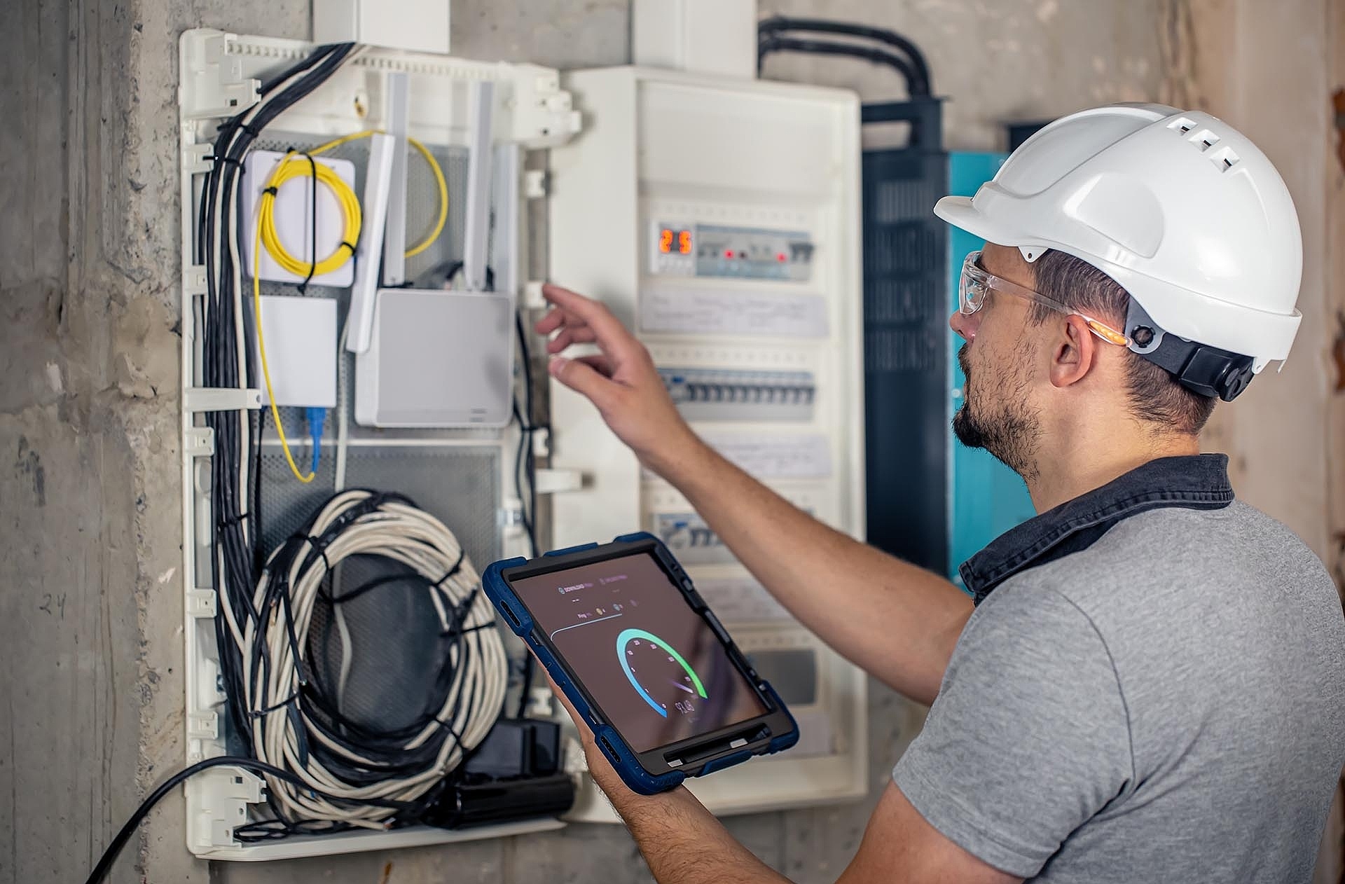 Man, an electrical technician working in a switchboard with fuses, uses a tablet.